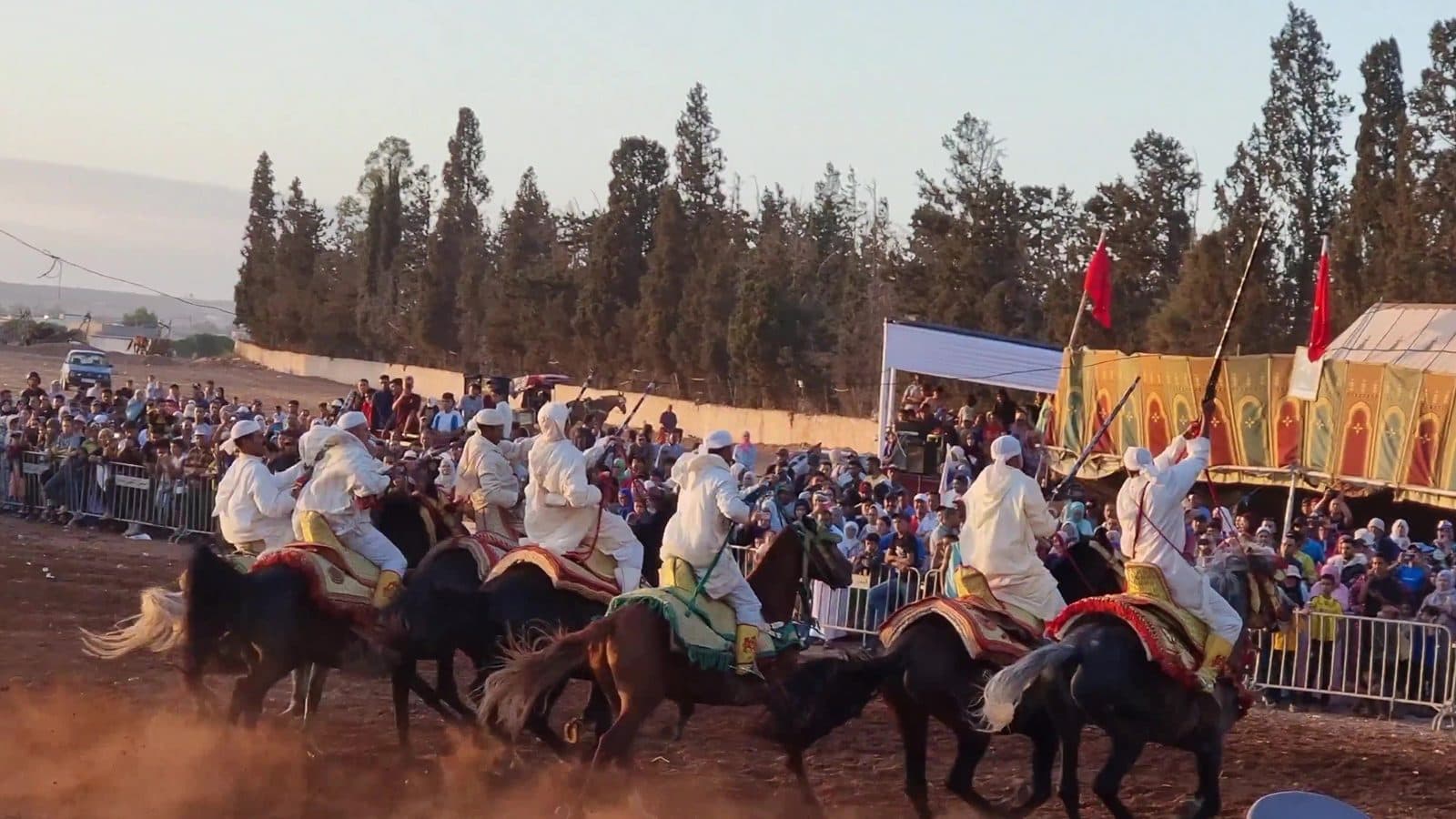 Crowd watching tbourida riders gallop past decorated tents at a moussem in rural Morocco
