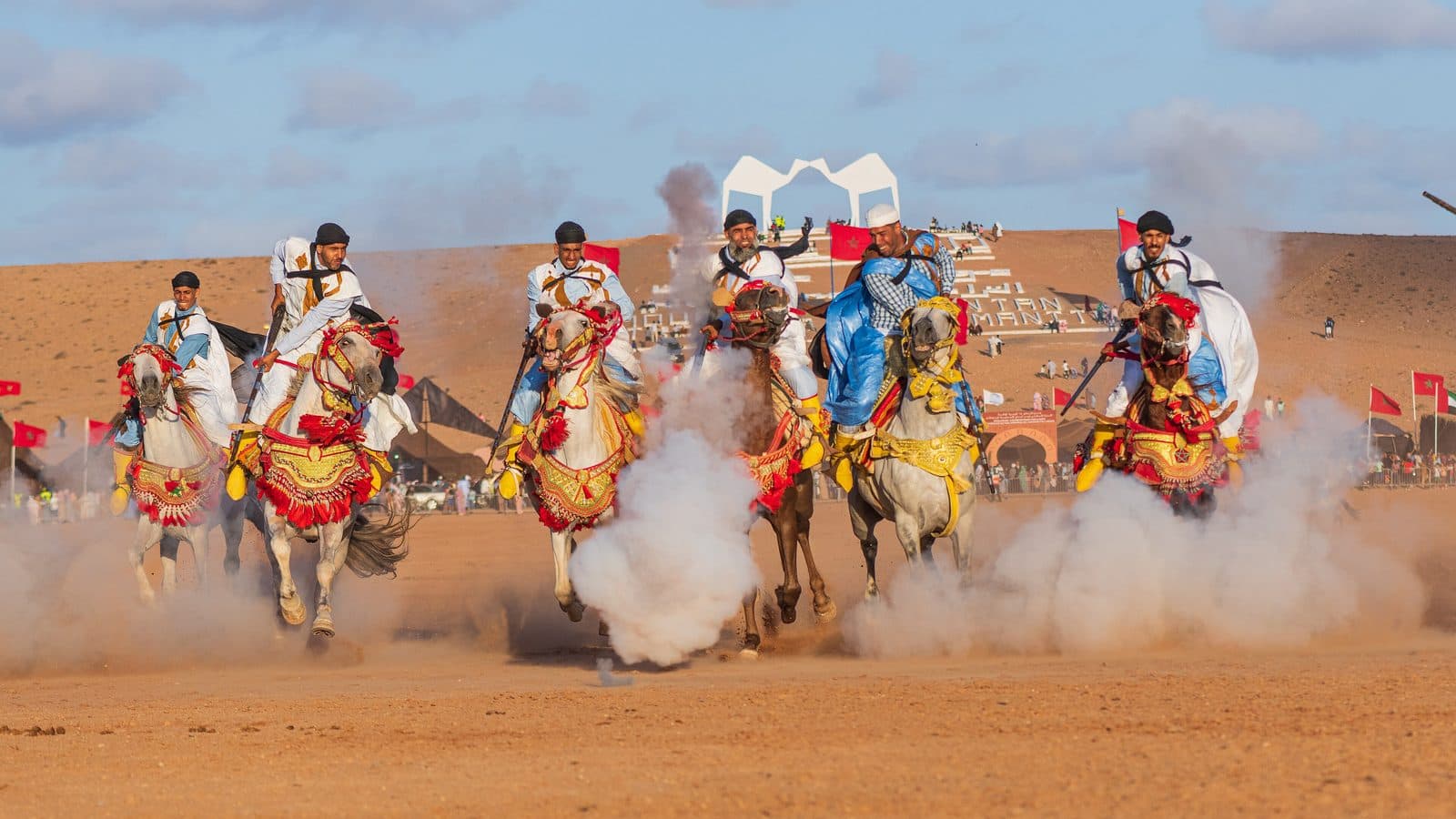 Riders in red, blue and white robes charging in a line during the Tan-Tan moussem