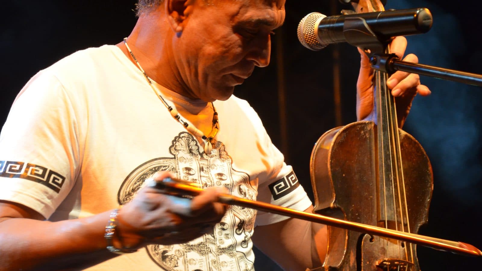 A Moroccan musician playing a violin held upright on his knee, Andalusian style, in front of a microphone