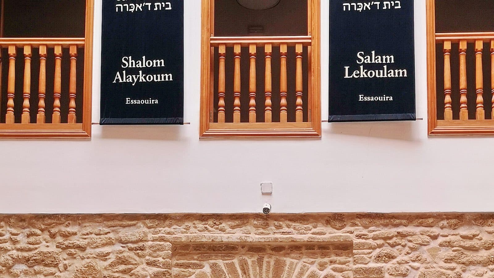 Balcons en bois et bannières noires « Shalom Alaykoum » et « Salam Lekoulam » au-dessus de la cour de Bayt Dakira