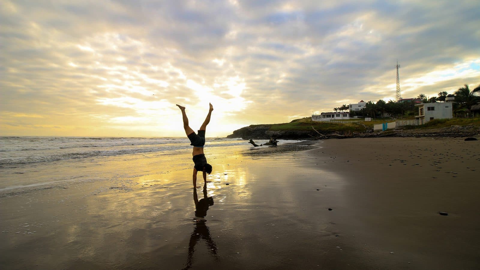 Person practising a handstand on a wet beach at sunrise