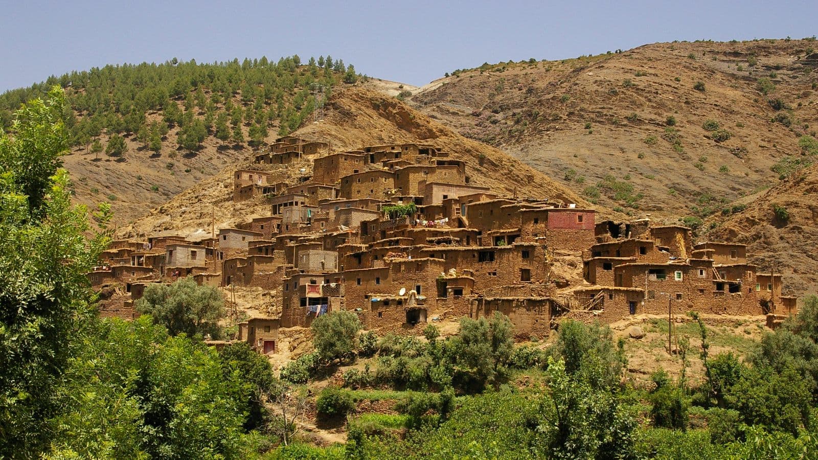 An earth-built Berber village on a green hillside in a High Atlas valley