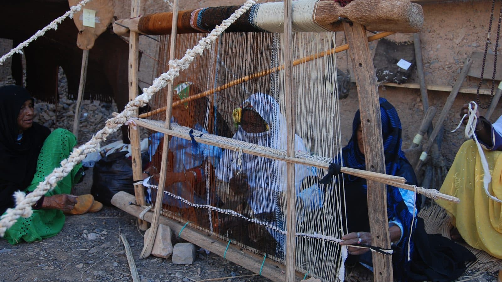 Moroccan women weaving a carpet on a large traditional wooden loom