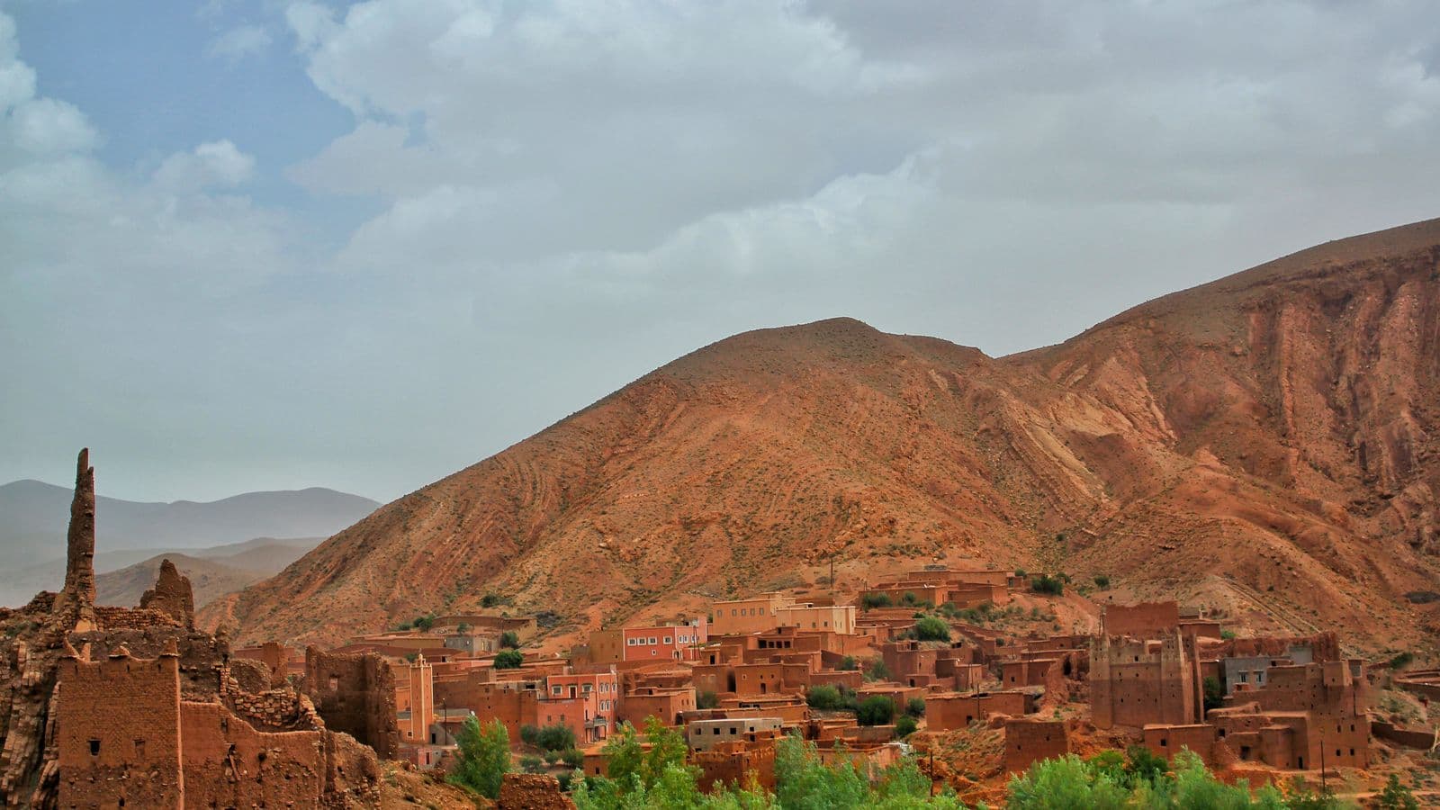An earth-built village and kasbah at the foot of red mountains in the Dades valley