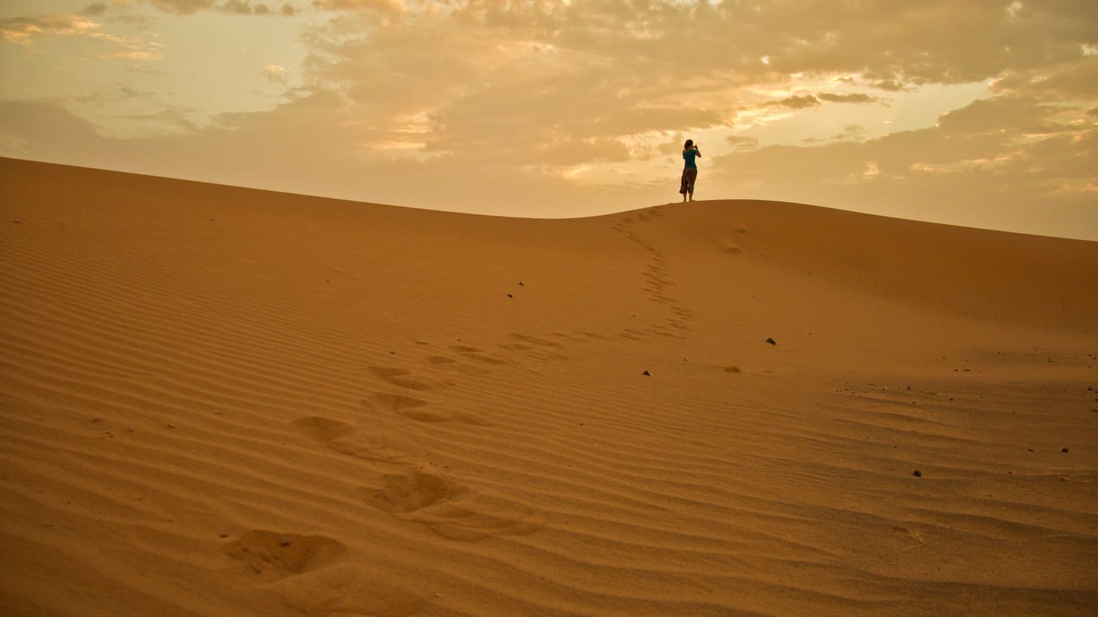 A lone walker on a dune crest watching the sunrise over the Erg Chebbi dunes