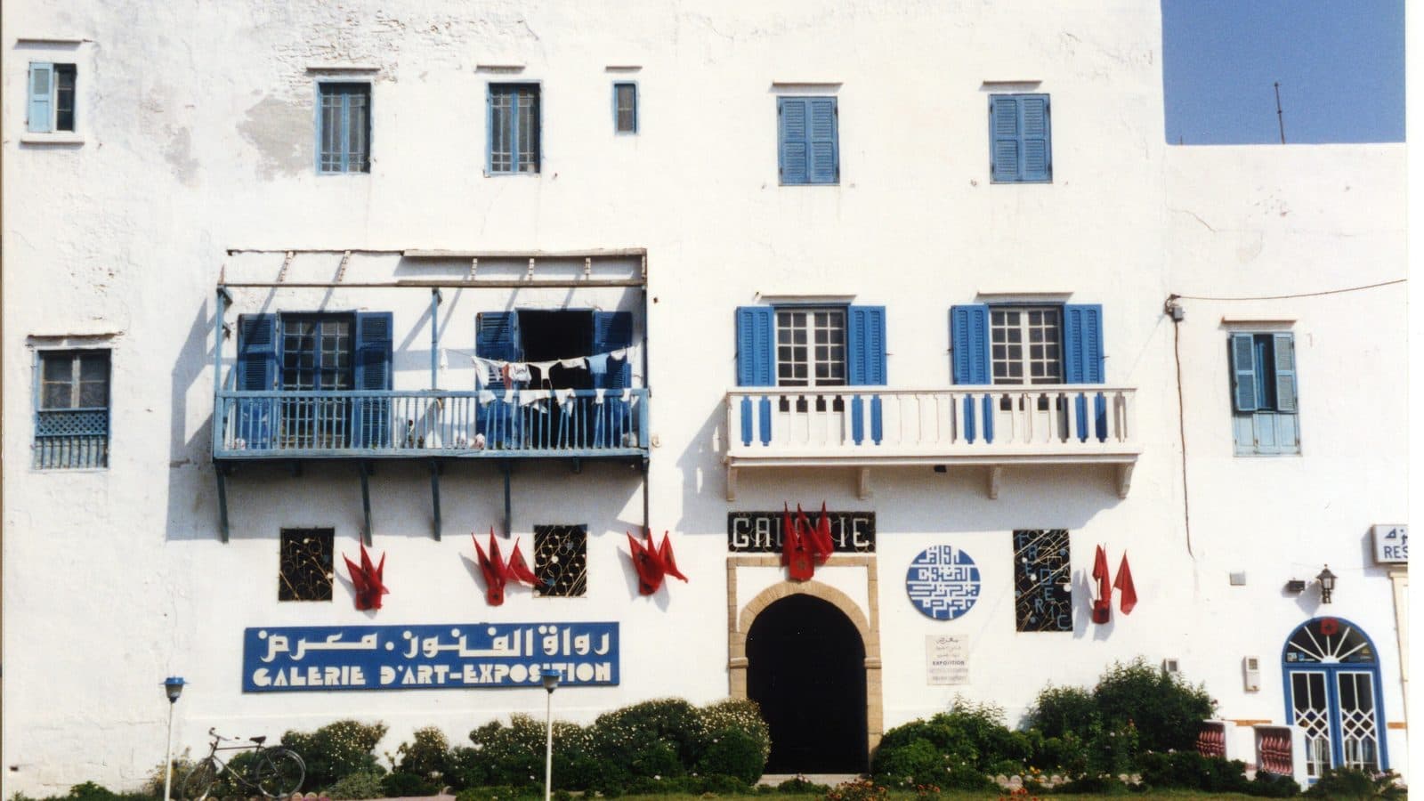 White façade with blue shutters of an art gallery and exhibition space in Essaouira