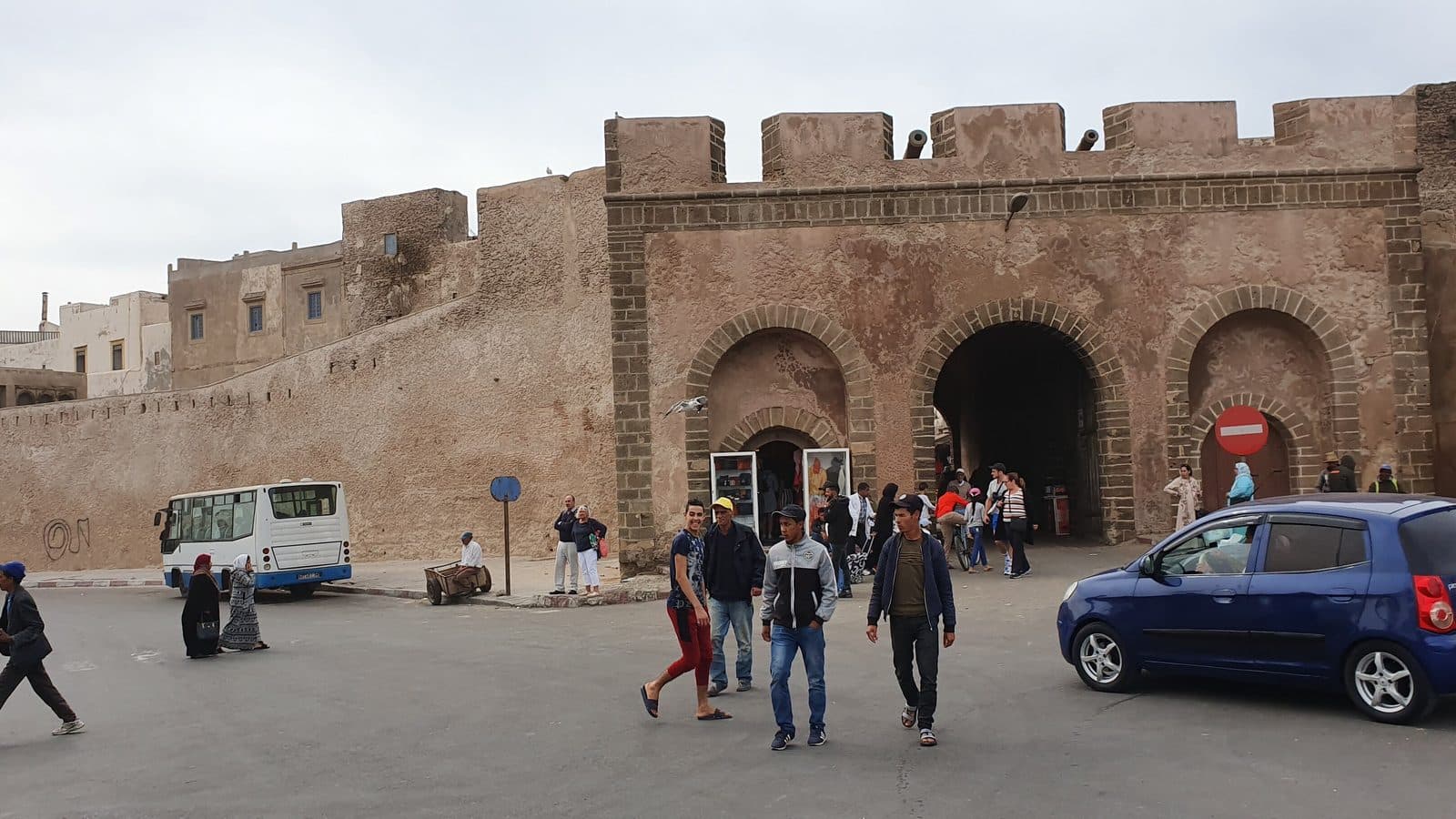 Voitures, minibus et piétons devant la porte crénelée de Bab Doukkala à Essaouira
