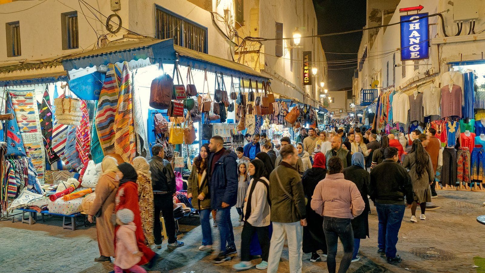 Crowds strolling past lit-up shops and rugs in the Essaouira medina at night
