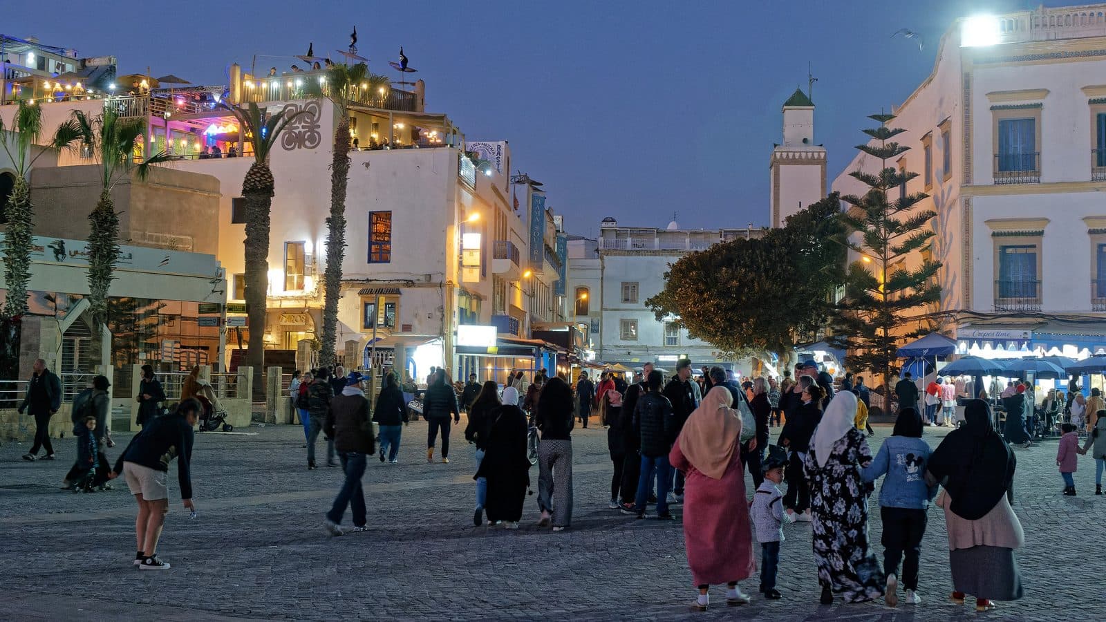 Evening crowd on Place Moulay Hassan in Essaouira with lit-up buildings and the minaret
