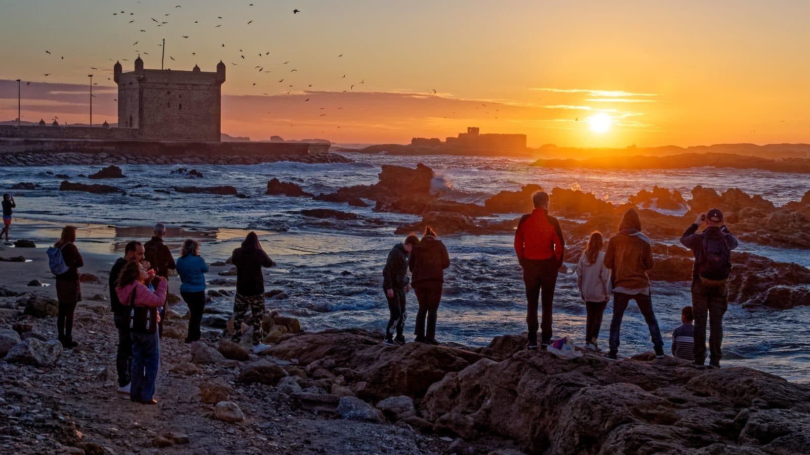 Visitors gathered on the rocks below the Skala of Essaouira at sunset