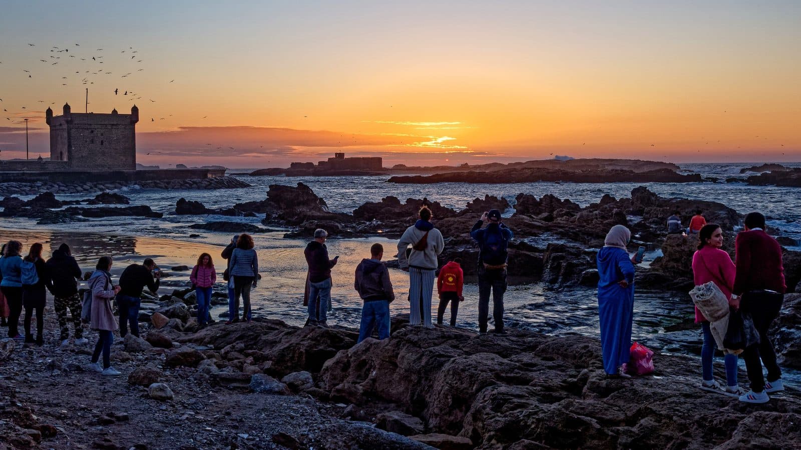 Groupe d’amis sur les rochers regardant le soleil se coucher derrière la Skala d’Essaouira