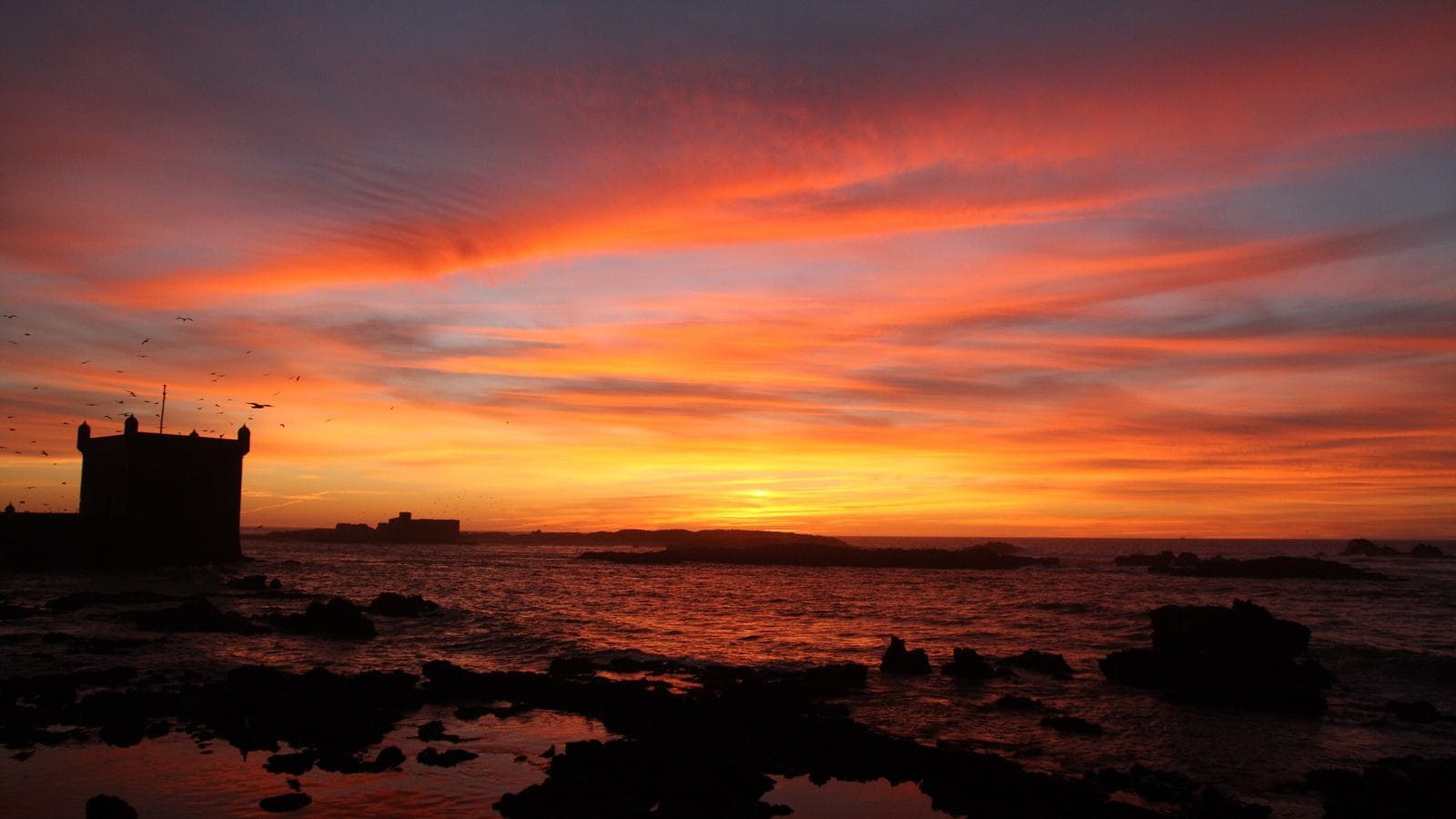 A fiery sunset over the sea and the silhouette of the Skala tower in Essaouira
