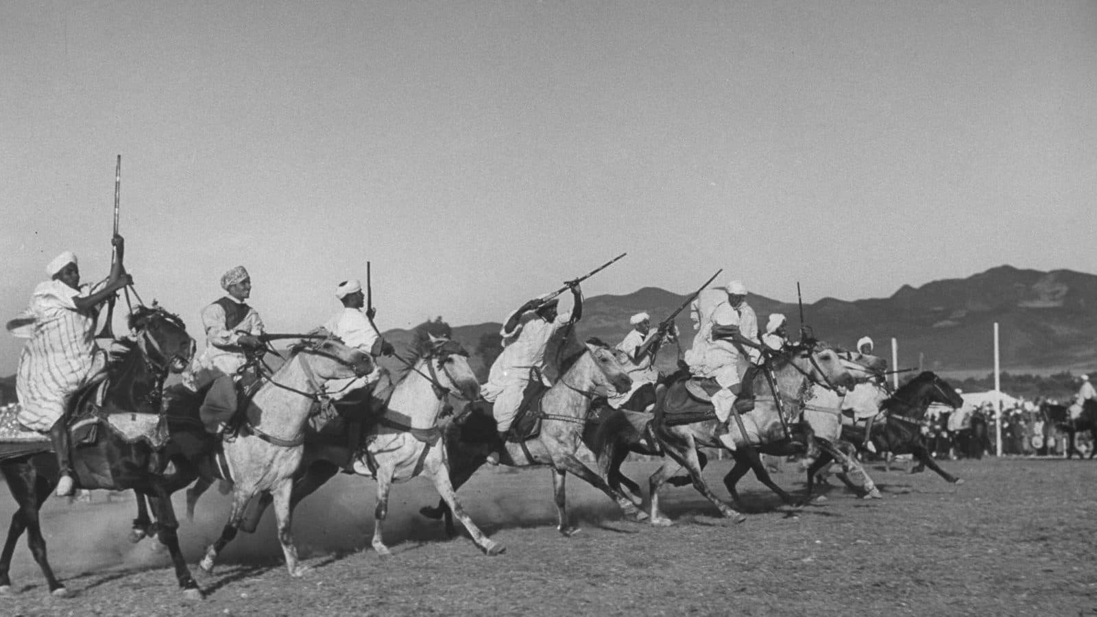 Photographie en noir et blanc de cavaliers chargeant fusils levés lors d'une fantasia à un mariage royal marocain en 1949