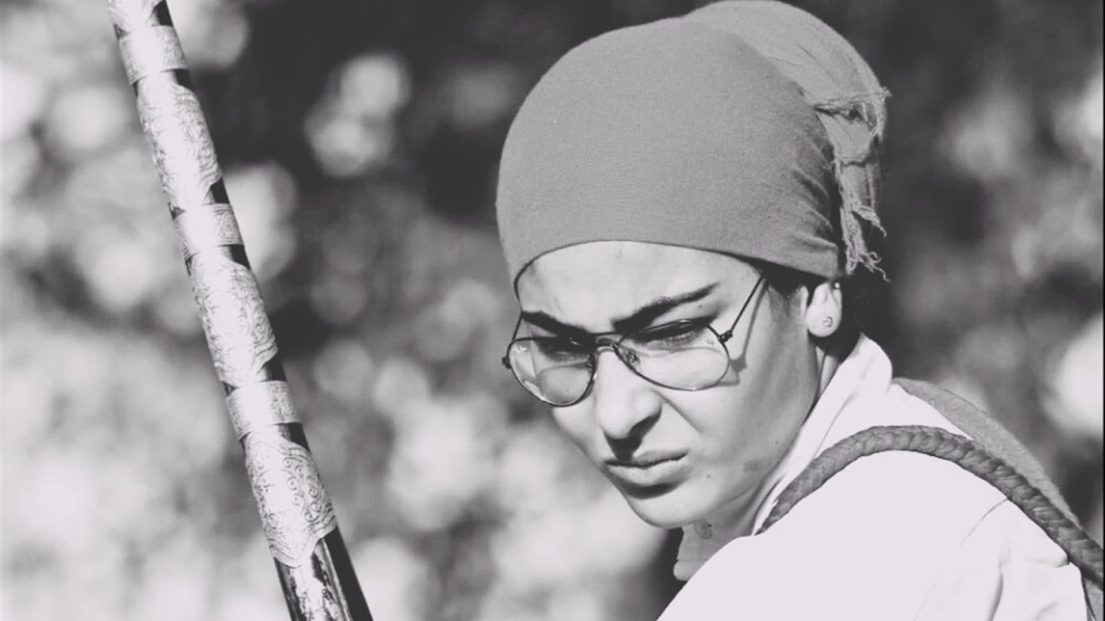 Black-and-white portrait of a young Moroccan woman in a headscarf holding a long musket during a fantasia