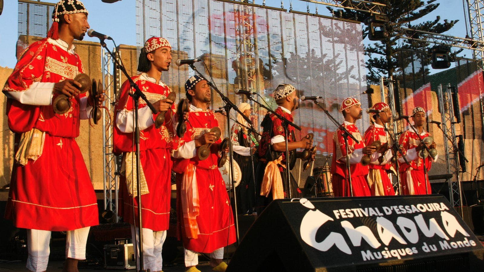 Gnawa musicians in red costumes playing qraqeb castanets on the stage of the Gnaoua festival in Essaouira