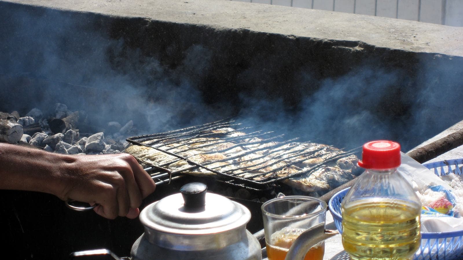 Sardines grillant sur un barbecue au charbon de bois fumant au Maroc, avec une théière à côté