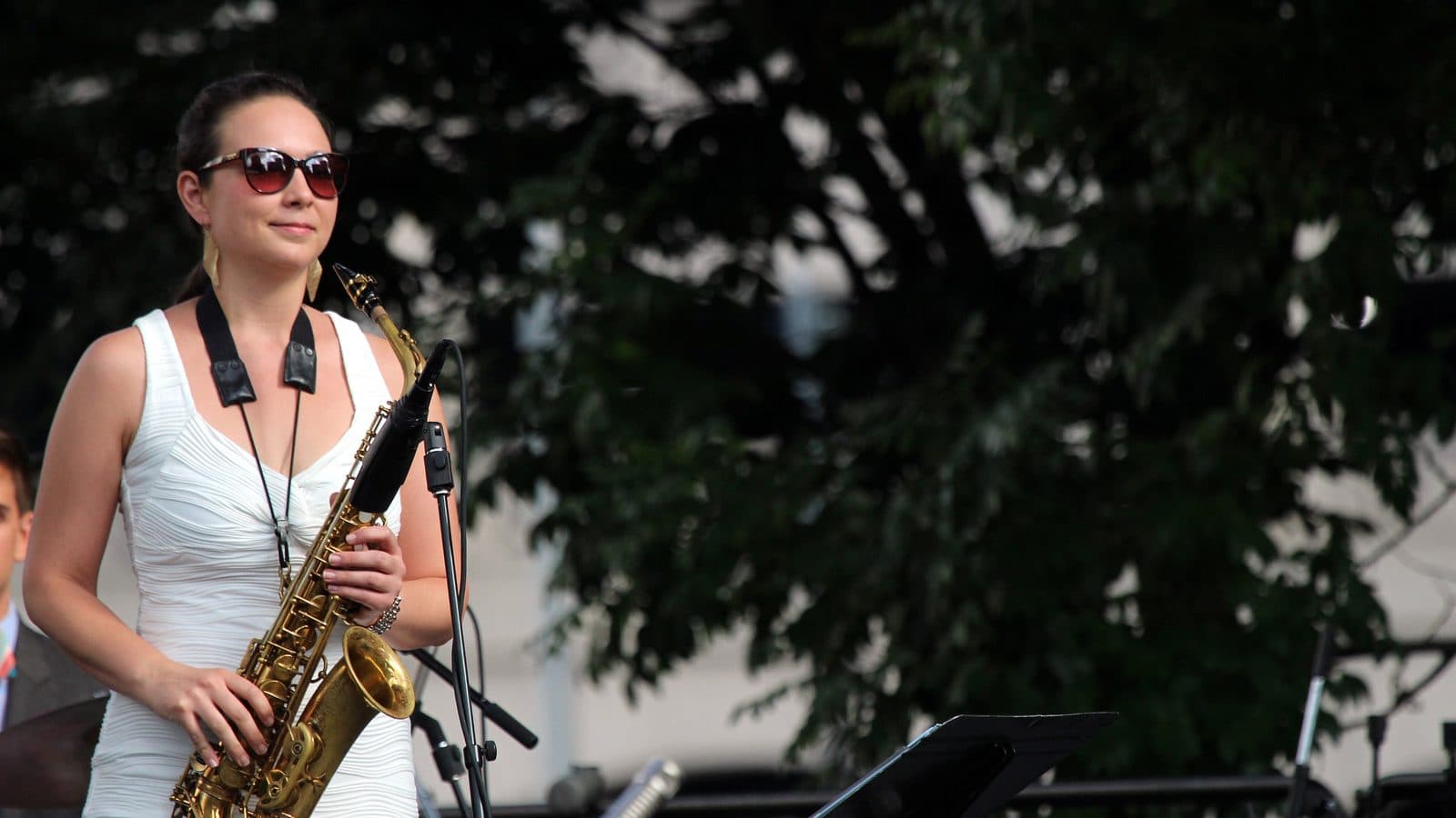 A saxophonist in sunglasses performing on an outdoor stage at a jazz festival