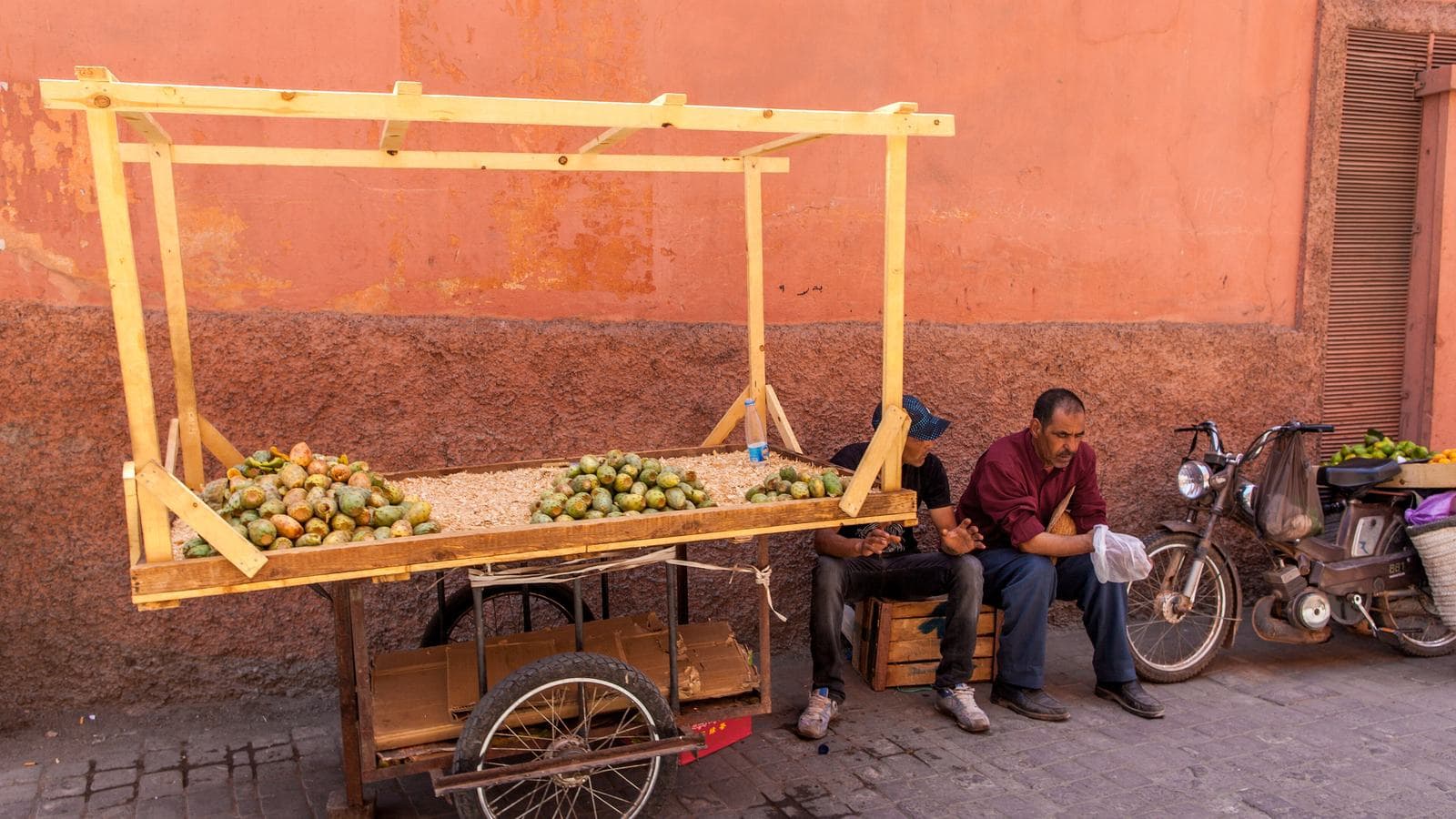 Deux hommes se reposant près d'une charrette de fruits dans une ruelle paisible et ensoleillée de la médina de Marrakech