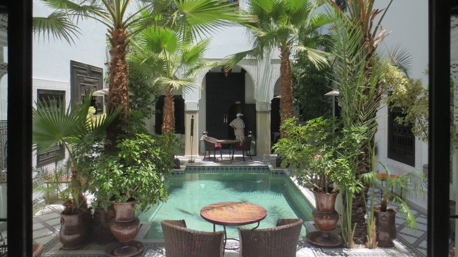 Un bassin entouré de palmiers et de plantes dans le patio d'un riad à Marrakech