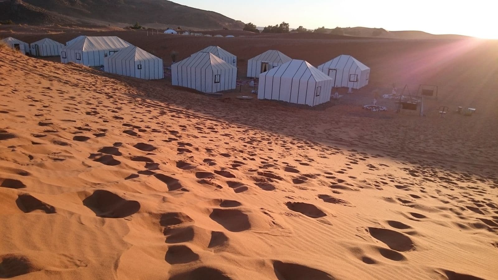 White tents of a desert camp at the foot of the Erg Chebbi dunes at sunset