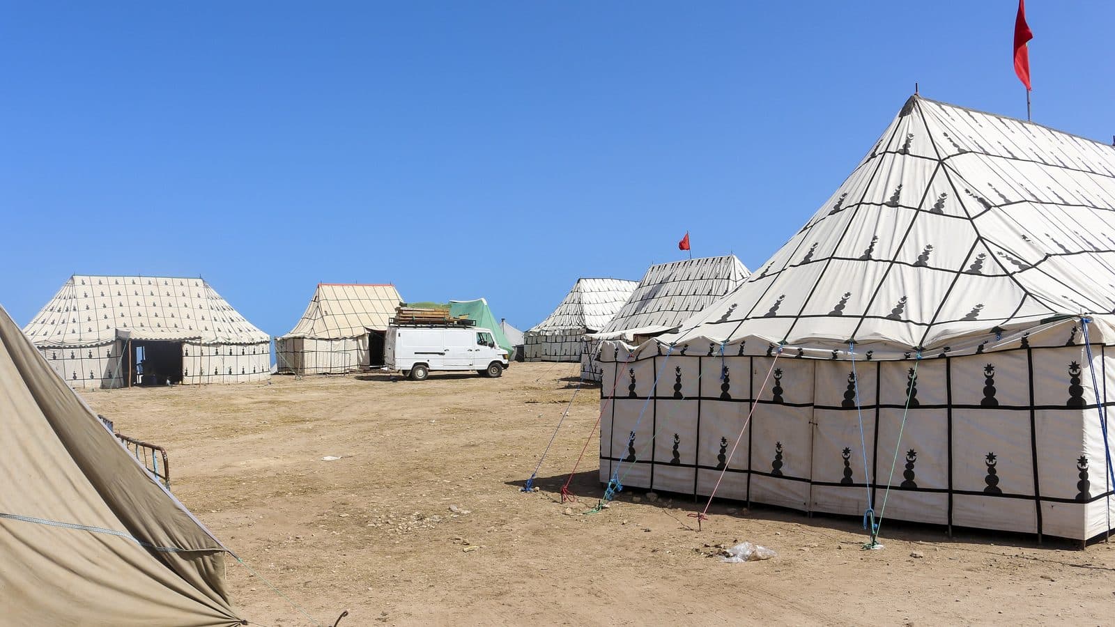 Large white Moroccan tents with black patterns set up for a moussem under a blue sky