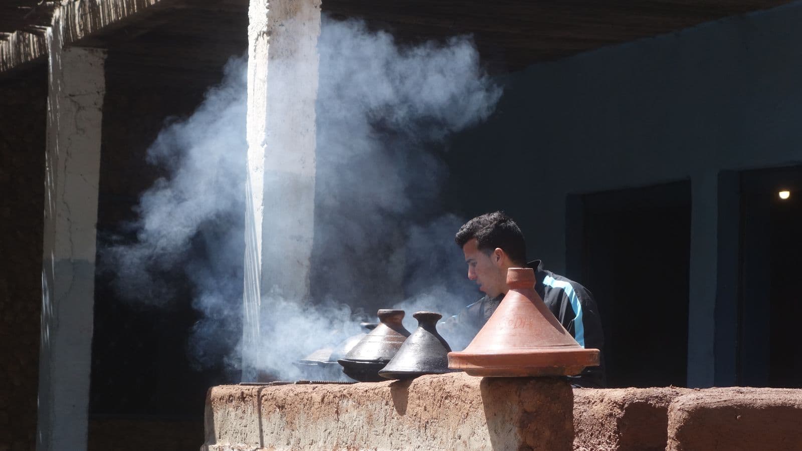 A cook standing in the steam of clay tagines simmering over charcoal