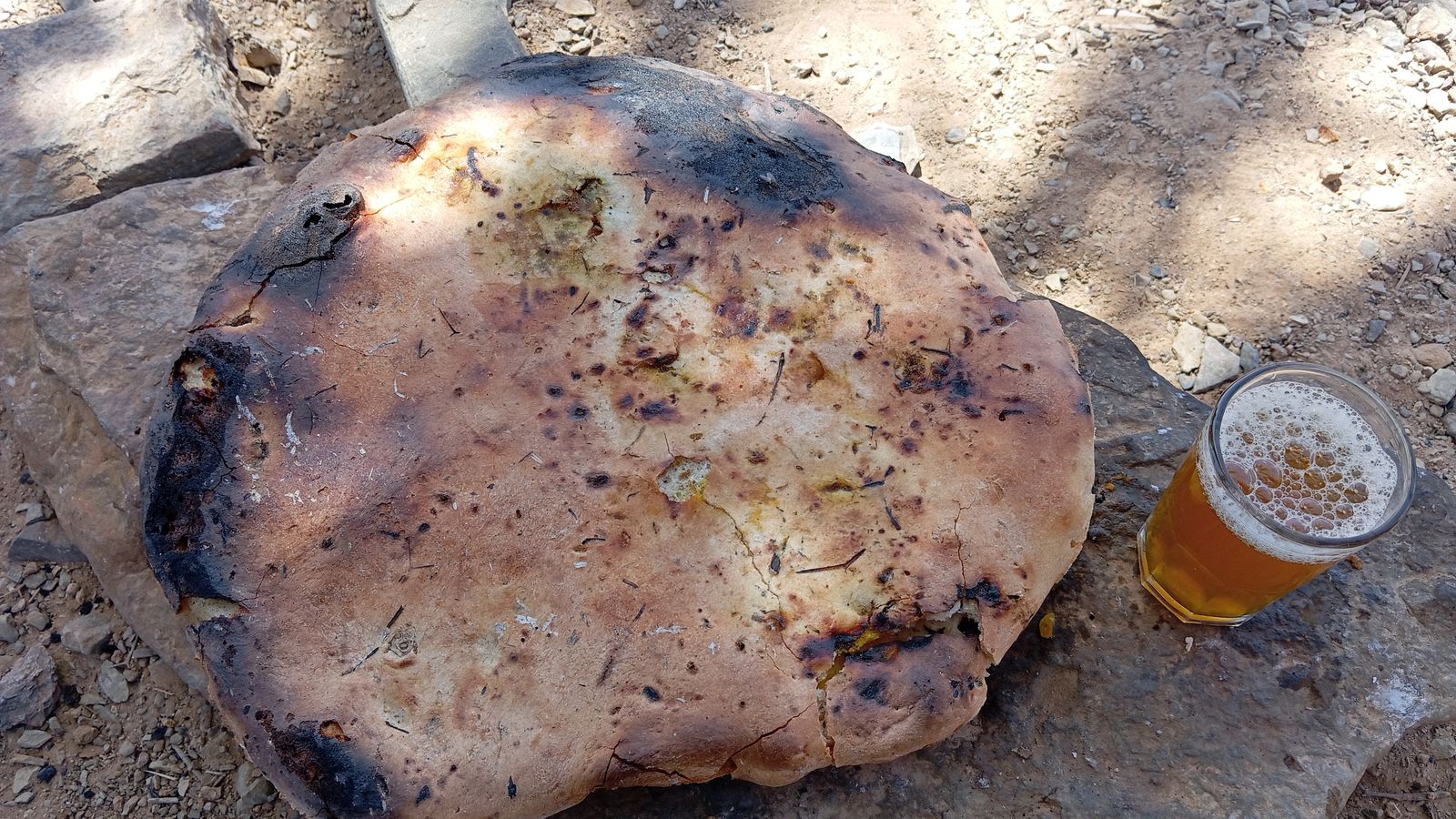 A round flatbread baked in the sand next to a glass of mint tea