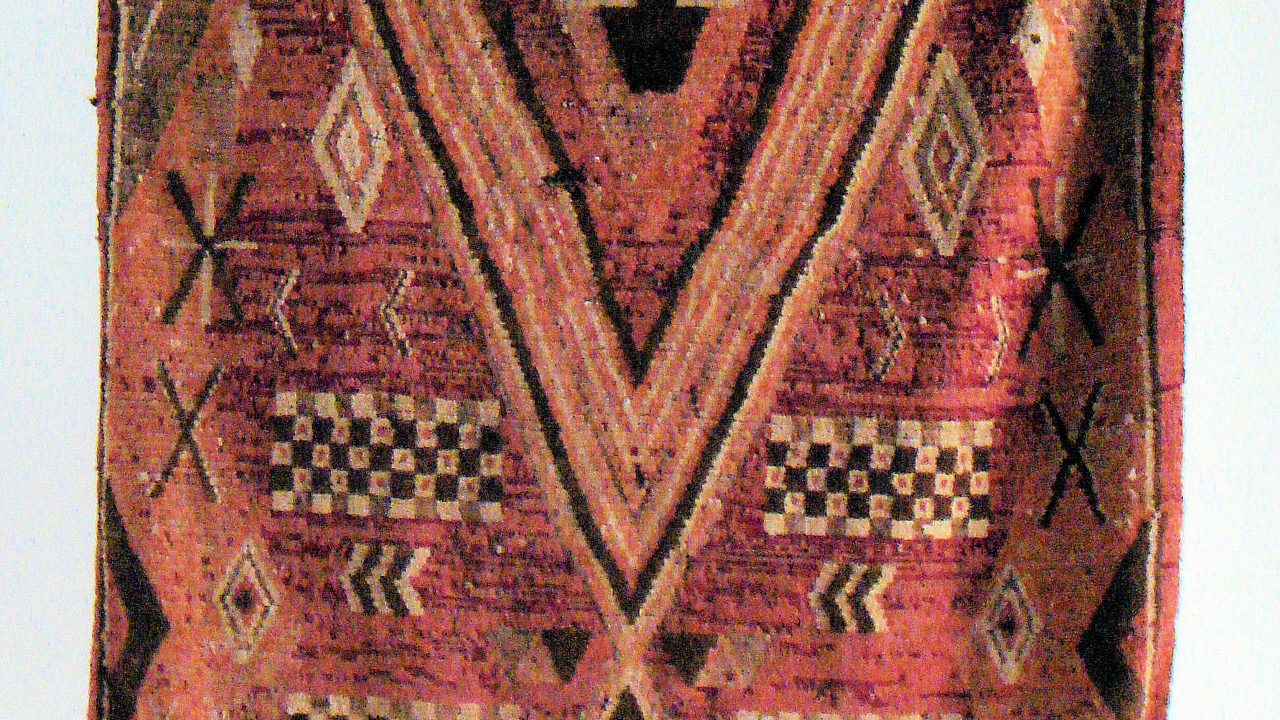 A Chichaoua rug with a red background, black and cream geometric motifs and a fringed edge