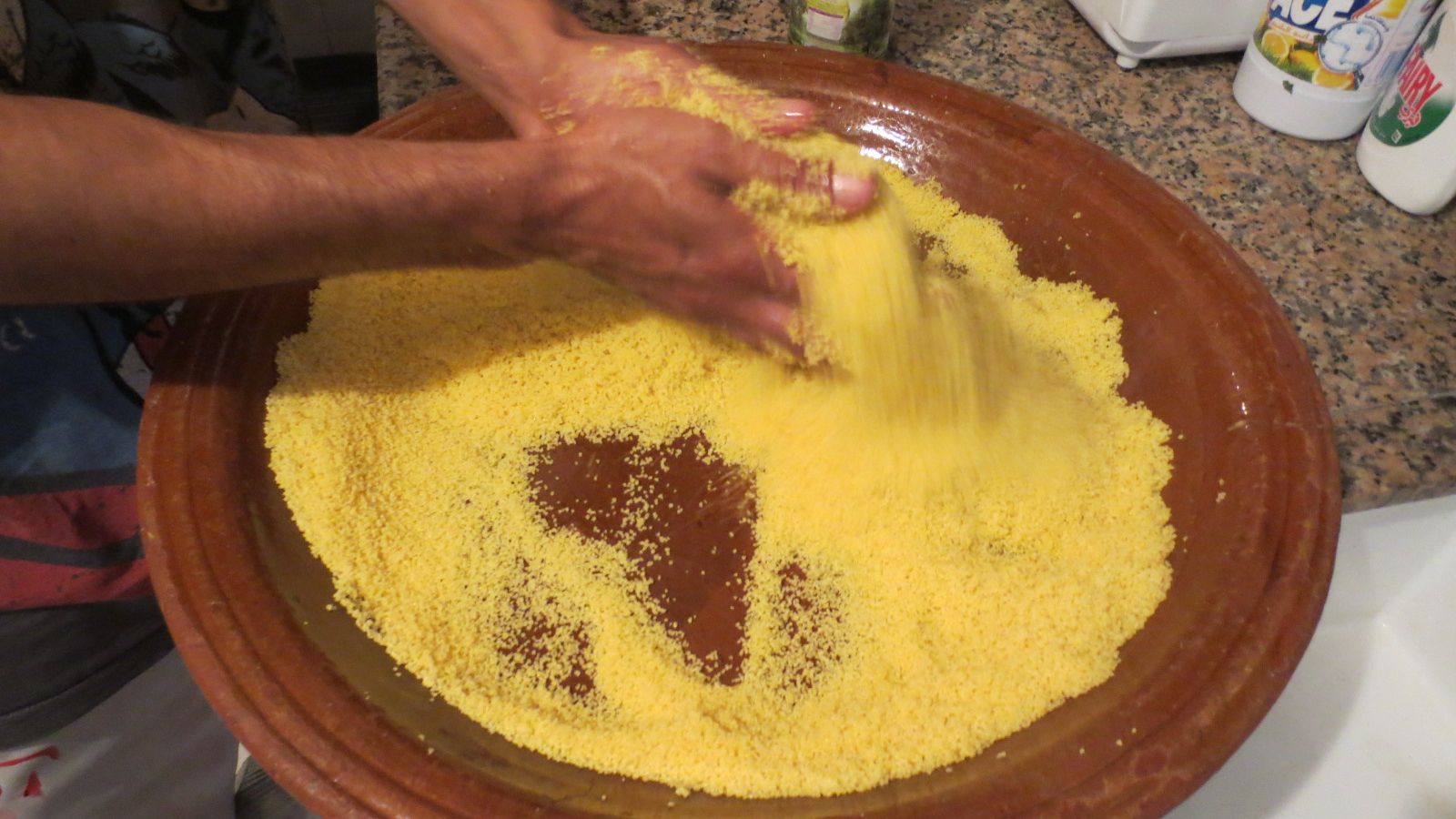 Hands rolling semolina grains for couscous in a large earthenware dish