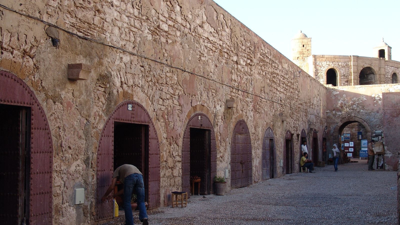 Boutiques en arcades sous le chemin de ronde des anciens remparts d'Essaouira, dans la douce lumière du soir