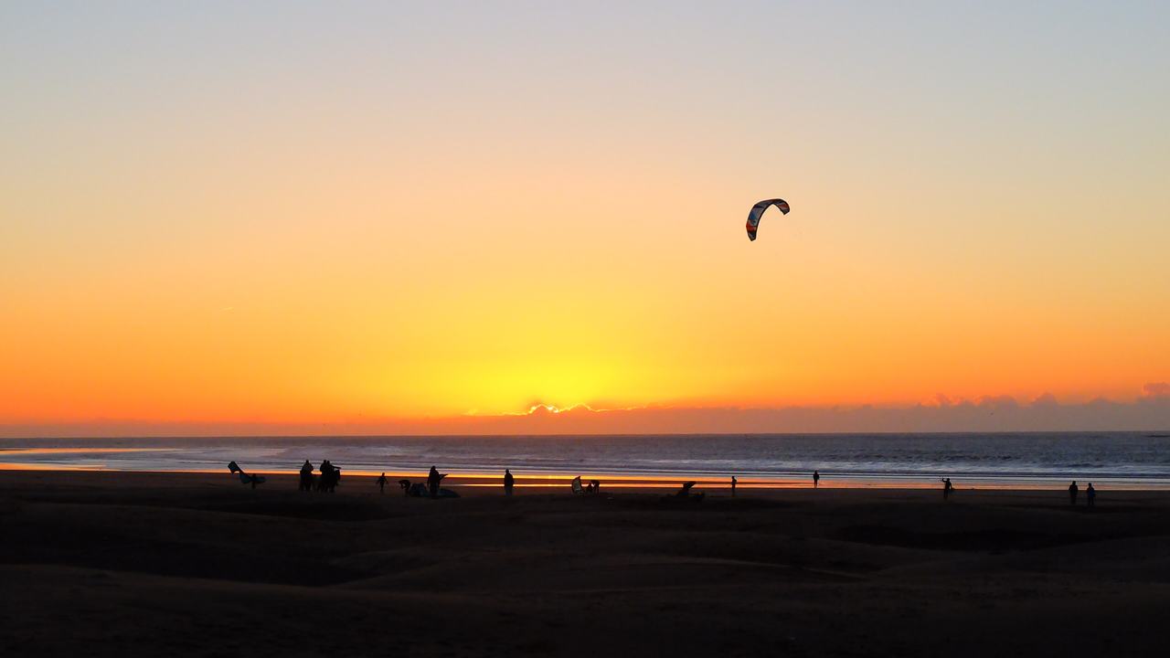 Une aile de kite en silhouette sur un coucher de soleil orangé au-dessus de la plage d'Essaouira