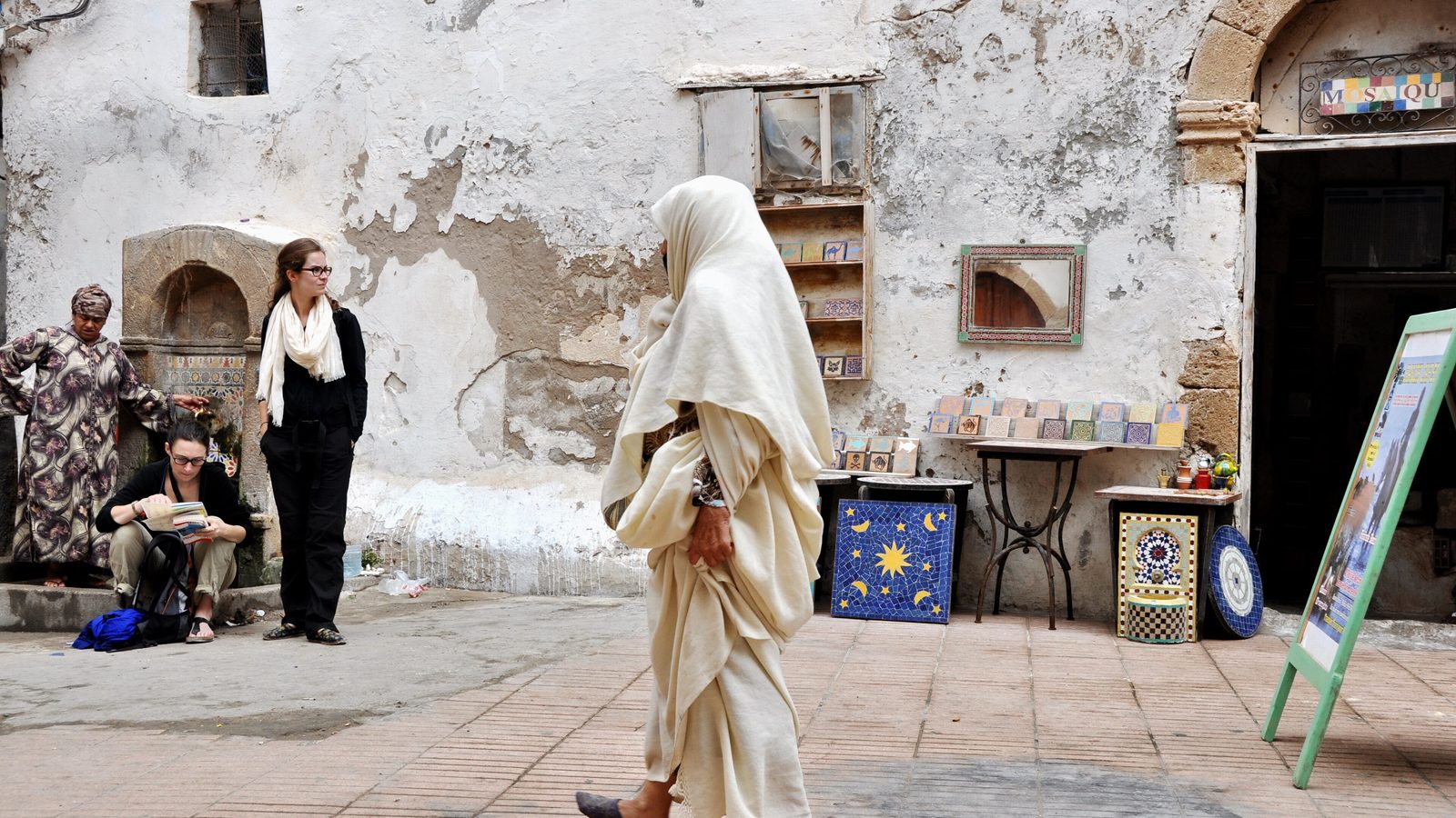 Une femme en haïk blanc traversant une petite place du mellah d'Essaouira
