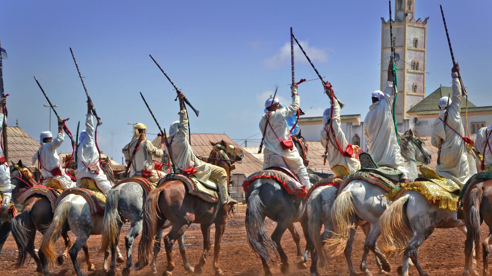 A fantasia charge with raised rifles in a village arena below a minaret
