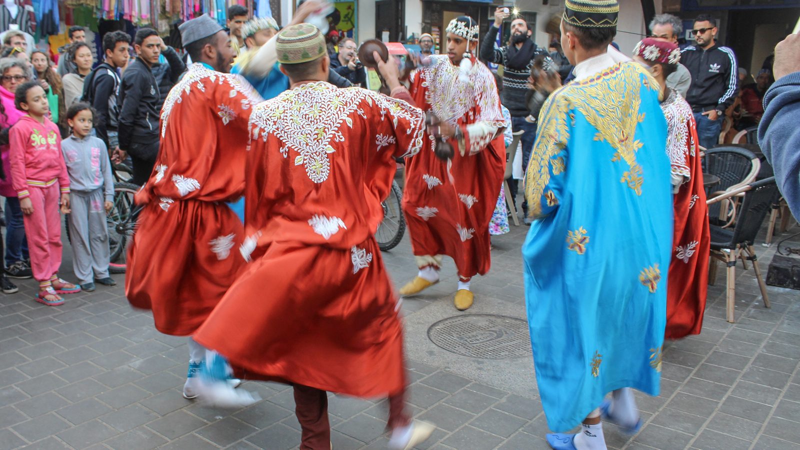 Musiciens gnaoua en tenues rouges et bleues dansant dans une rue de la médina d'Essaouira