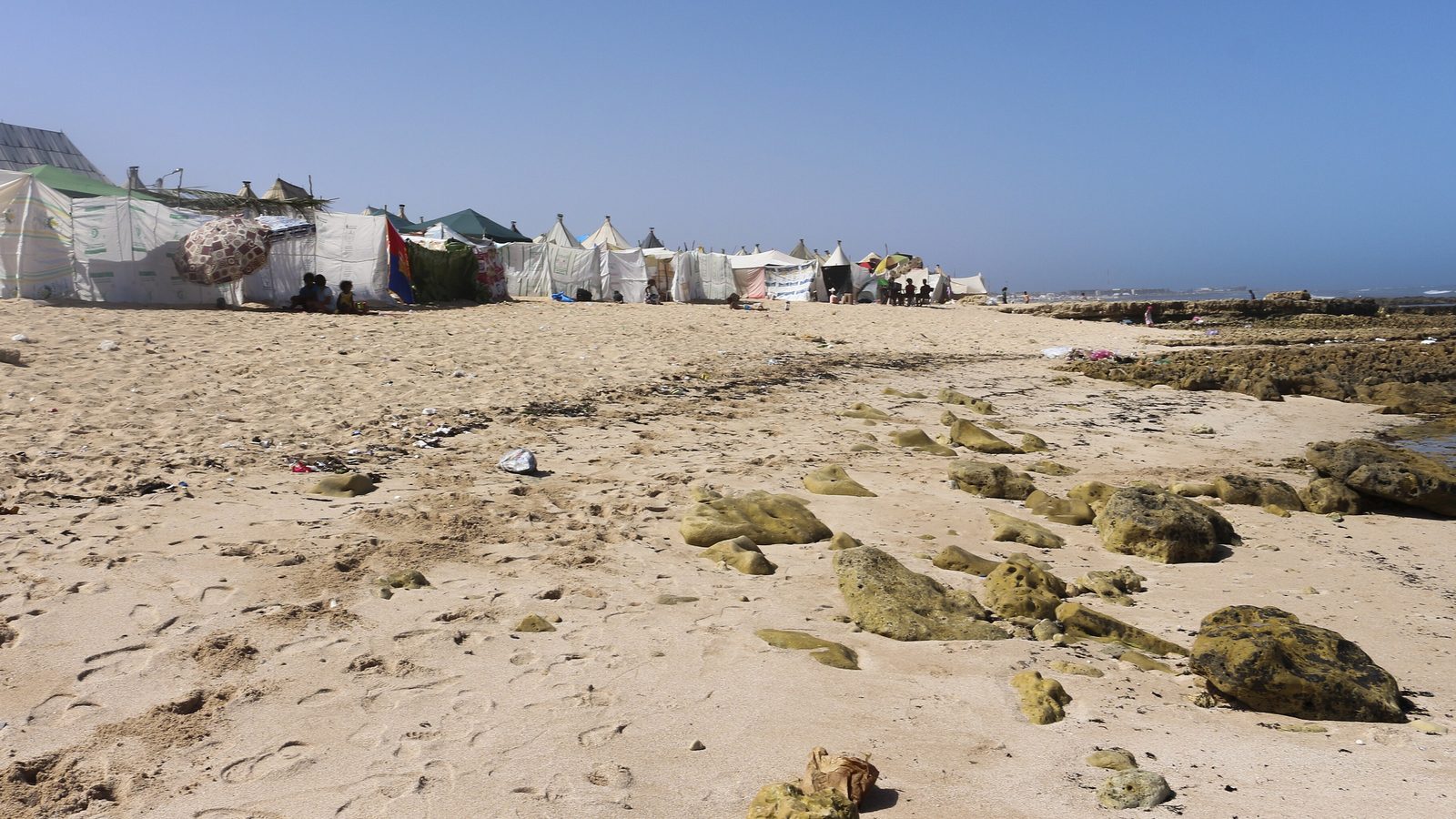 White tents lined up behind a sandy, rocky beach during the moussem of Moulay Abdallah Amghar
