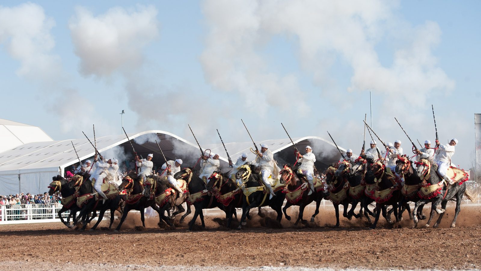 Tbourida riders charging in front of white grandstand tents at the Salon du Cheval in El Jadida