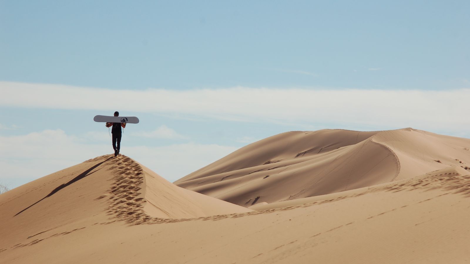 Un sandboardeur debout sur la crête d'une dune